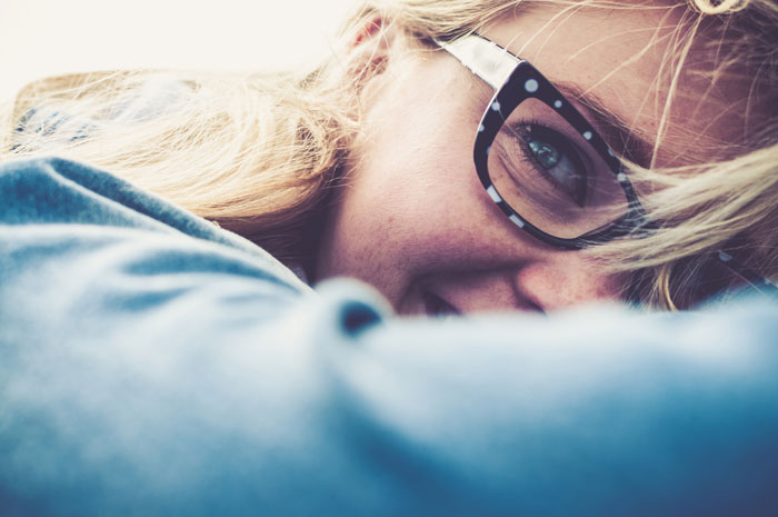 young blonde woman playfully smiling and hiding half of her face wearing fun eyeglasses