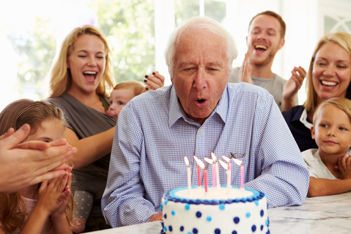 grandfather blowing out birthday cake candles at a birthday party with family Signing up for medigap coverage at 65